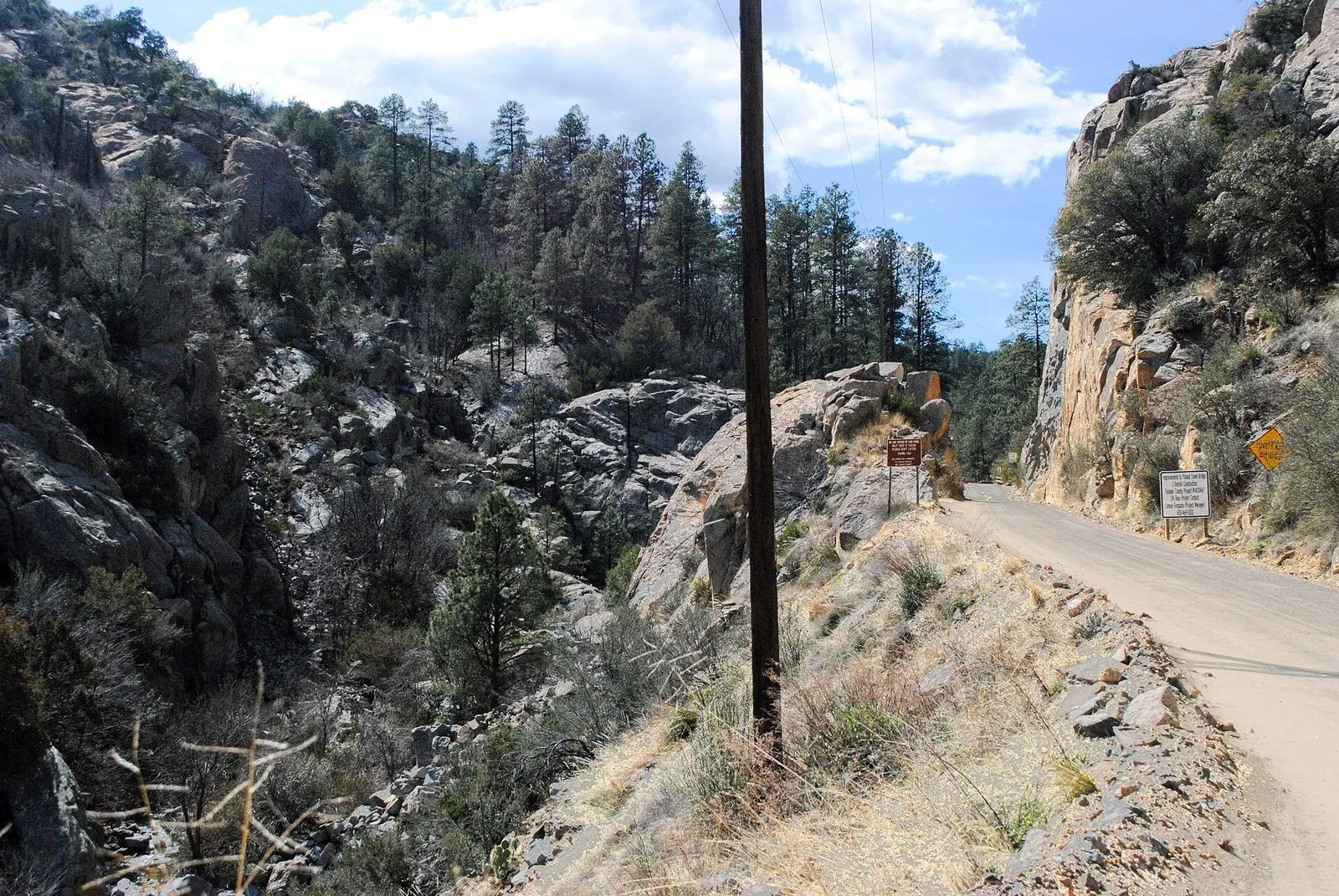 A narrow dirt road cut into a rocky hillside climbing through the Bradshaw Mountains toward Crown King