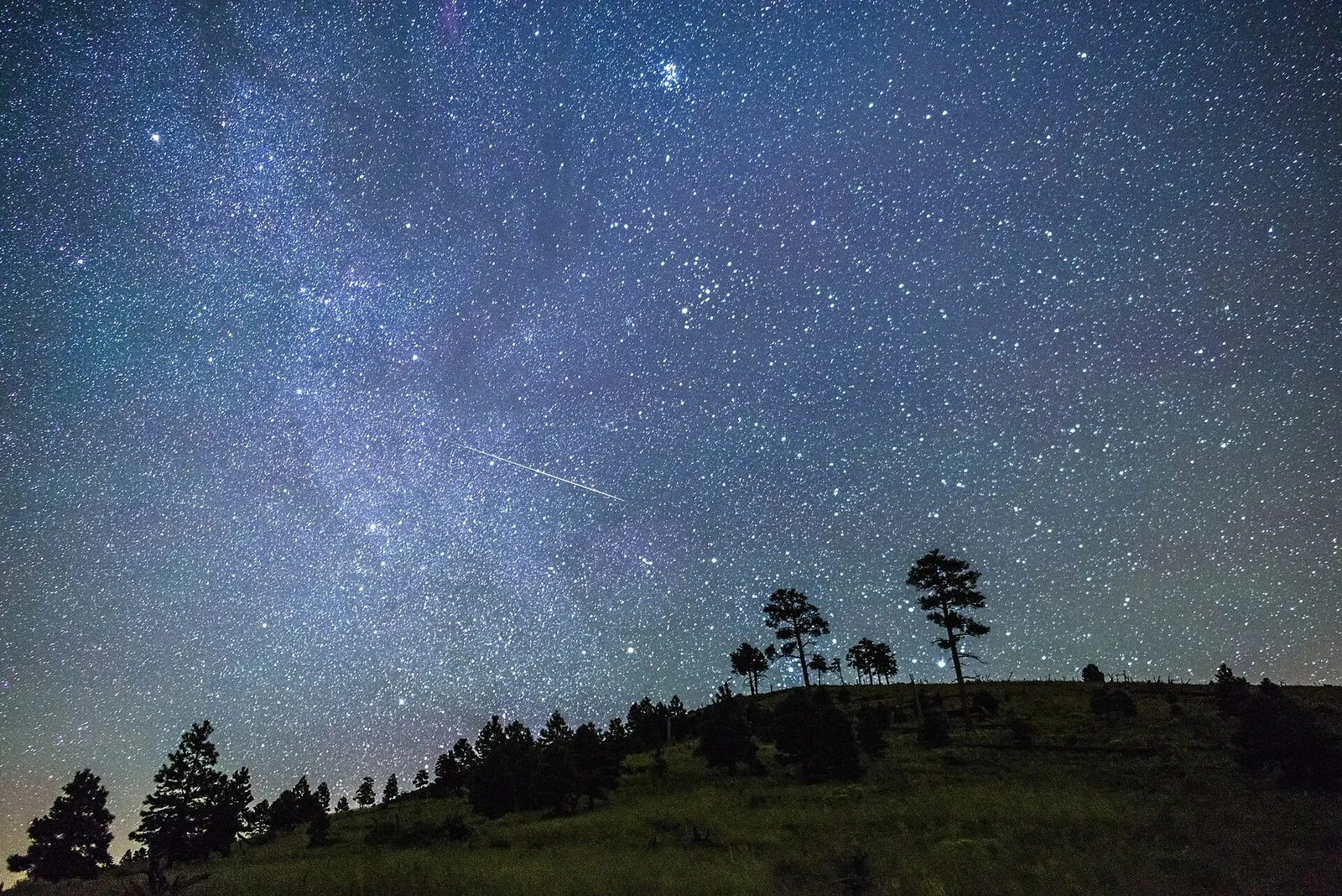 The Milky Way and a meteor over a dark pine-covered ridge in northern Arizona
